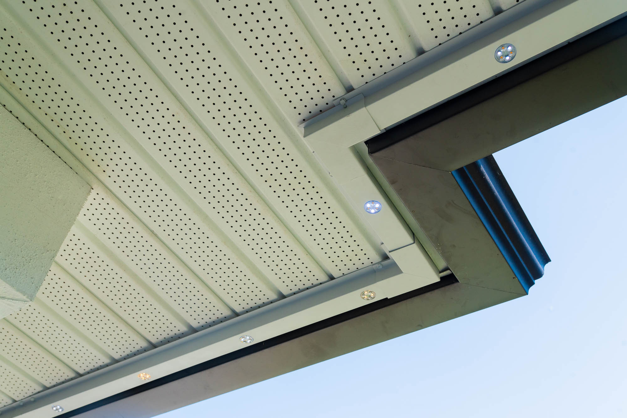 Close-up of low-profile LED nodes sitting flush on a white soffit in daylight
